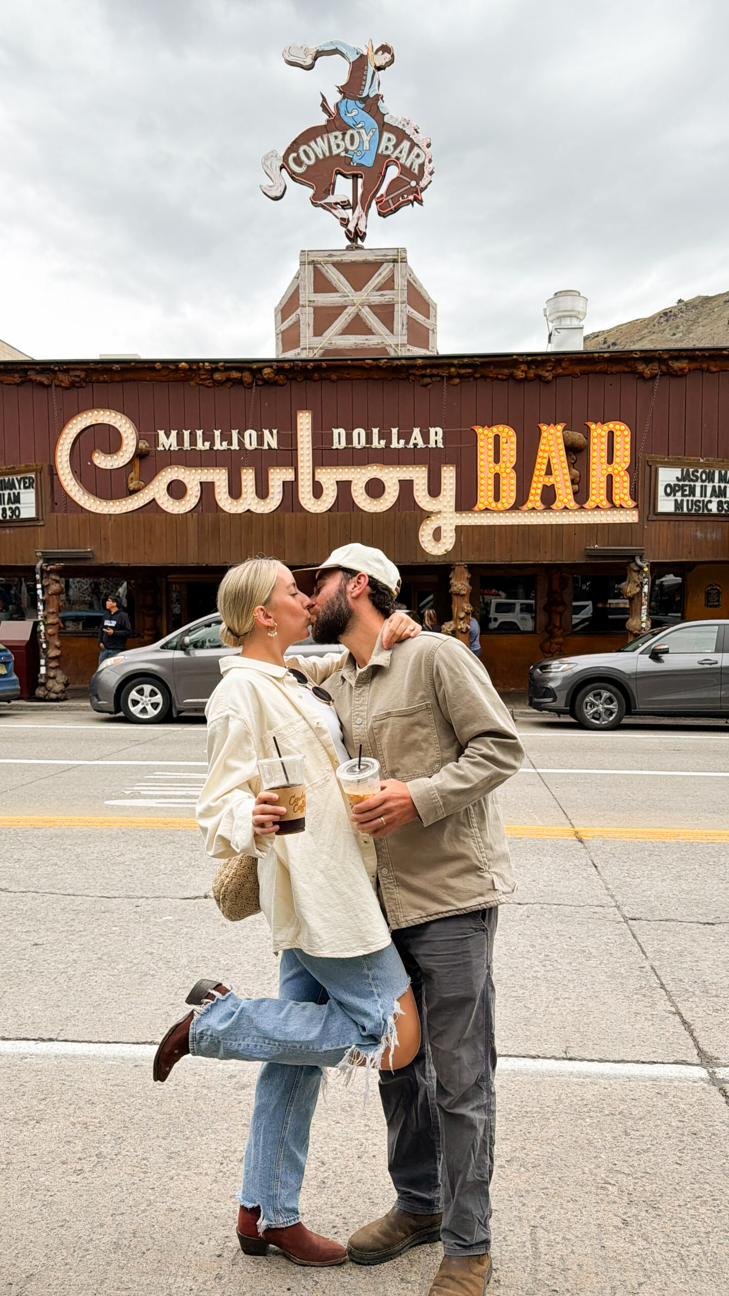 Couple kissing on the street in downtown Jackson Hole with the Million Dollar Cowboy Bar sign lit up behind them