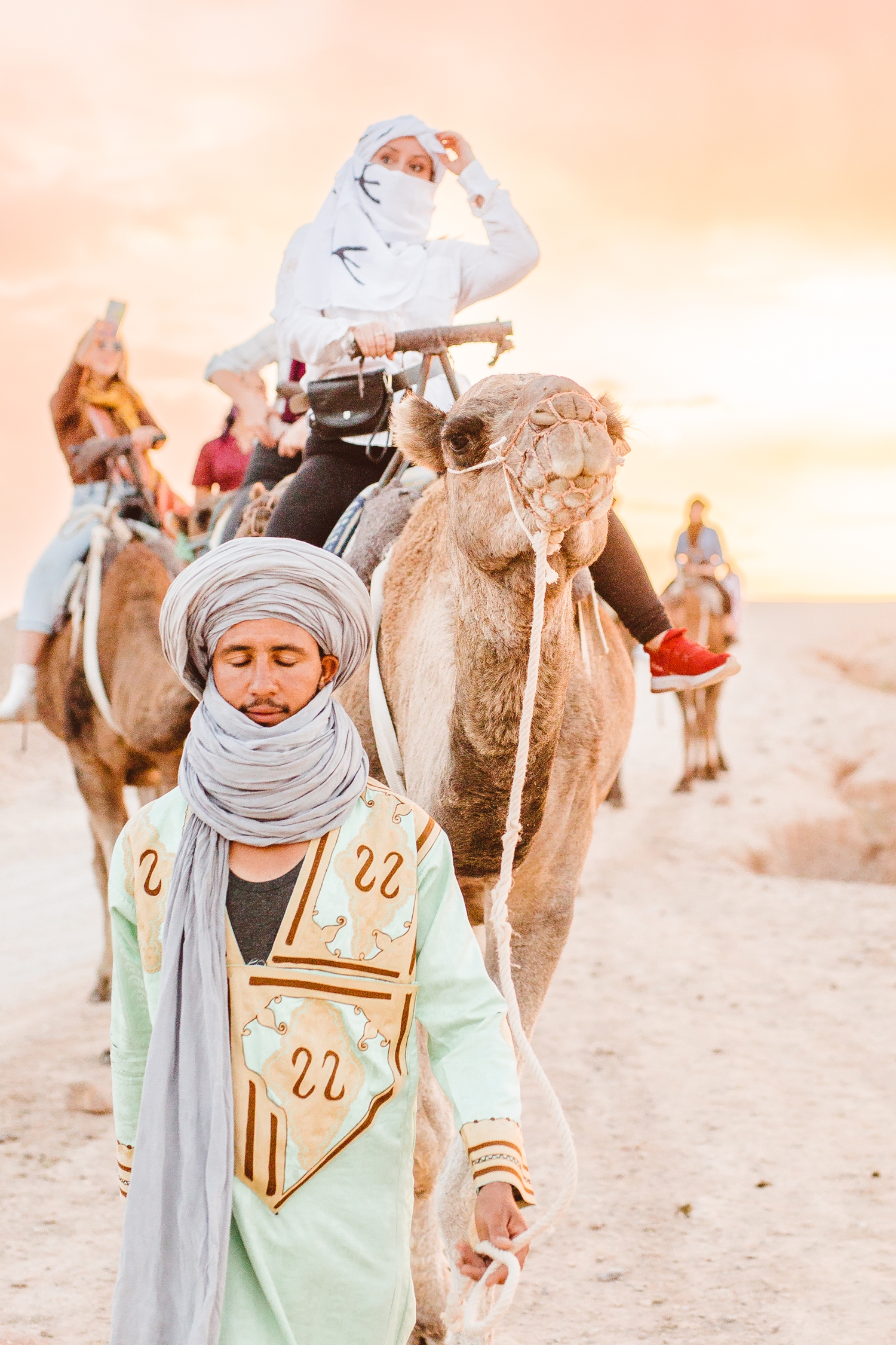 Man leading group of women riding camels in Afgay Desert in Morocco | Brooke Michelle Photography