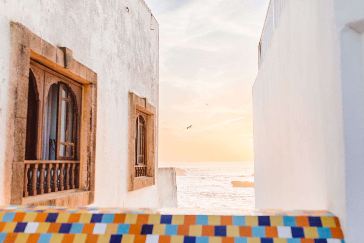 Peak of the ocean through two white buildings and a colorful wall in Marrakesh, Morocco | Brooke Michelle Photography