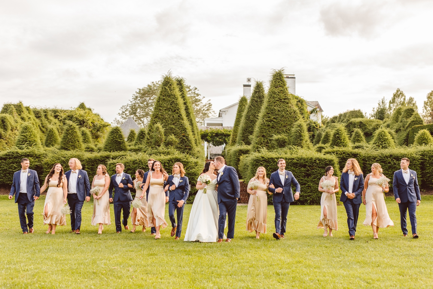 Wedding party walking while bride and groom kiss at Ladew Topiary Gardens | Brooke Michelle Photo