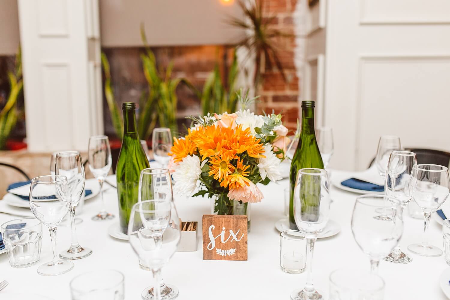 Reception table with orange and white bouquet, table number, and water glasses | Brooke Michelle Photography
