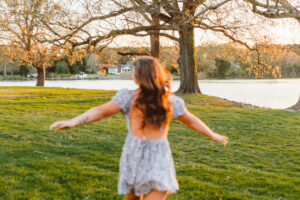 senior running on a field during her whimsical senior session with the sun in the background