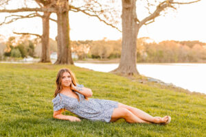 beautiful senior laying on the grass during her photoshoot with trees and the sun in the background
