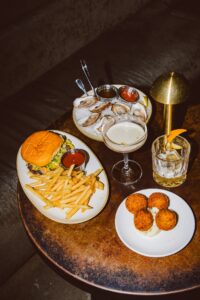 Table spread of oysters, burger, fries, and craft cocktails at a Bentonville, Arkansas restaurant, perfect for date-night photography