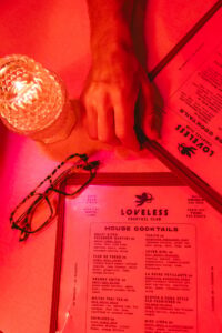 Reading the house cocktails menu under red neon light at Loveless Cocktail Club in downtown Bentonville, Arkansas