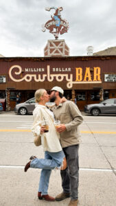 Couple kissing on the street in downtown Jackson Hole with the Million Dollar Cowboy Bar sign lit up behind them