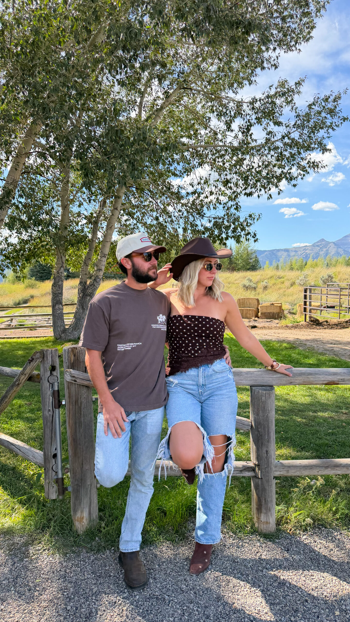 Couple leaning against a wooden ranch fence with the Grand Tetons in the distance, a scenic Jackson Hole engagement photo location