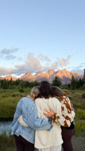 Three friends embracing while watching an alpenglow sunset over the Grand Teton mountain range