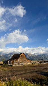 Historic wooden barn at Mormon Row with the Grand Teton mountain range and dramatic clouds behind it