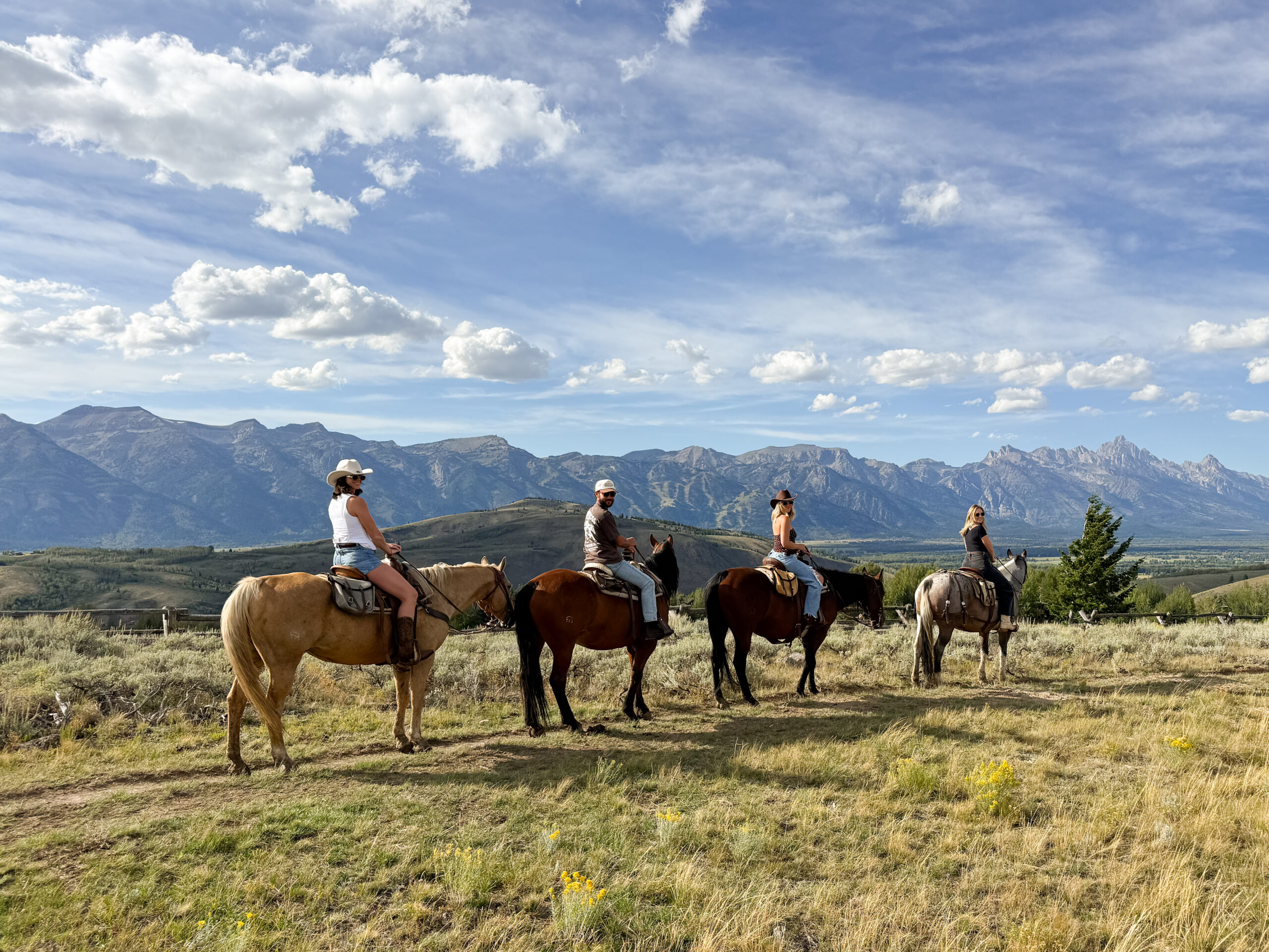 Group of four riders on horseback lined up on a ridge with the Grand Teton mountain range stretched out behind them